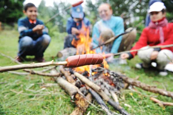 Barbecue in nature, group of people preparing sausages on fire (note shallow dof)